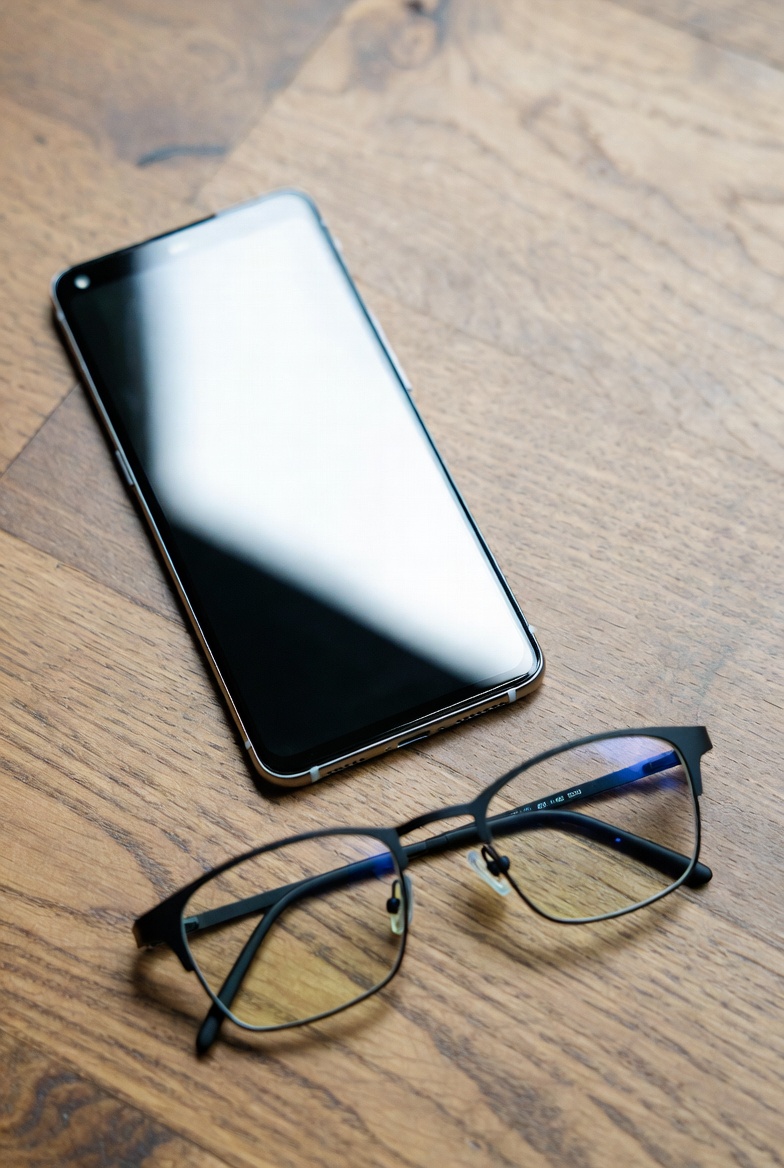 Person holding a smartphone next to slim smart glasses on a table